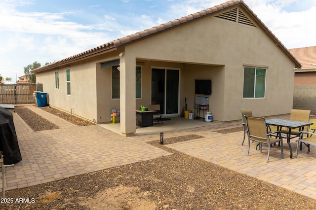rear view of house with stucco siding, a patio area, outdoor dining area, and fence