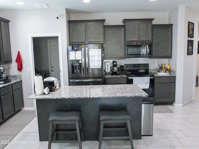 kitchen featuring stainless steel microwave, a kitchen bar, light stone countertops, fridge with ice dispenser, and electric stove