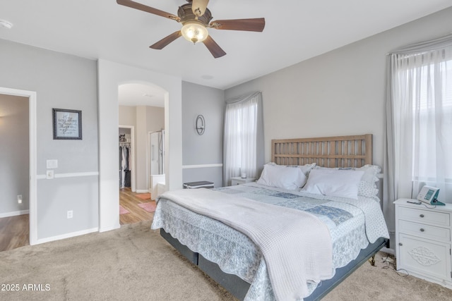 bedroom with light carpet, a walk in closet, a closet, and ceiling fan