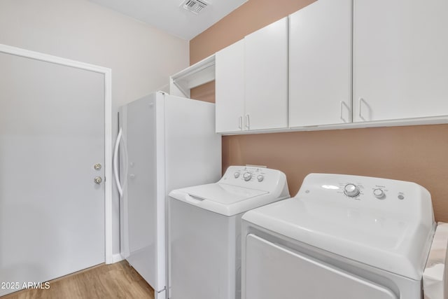 laundry room featuring cabinets, washing machine and dryer, and light hardwood / wood-style flooring