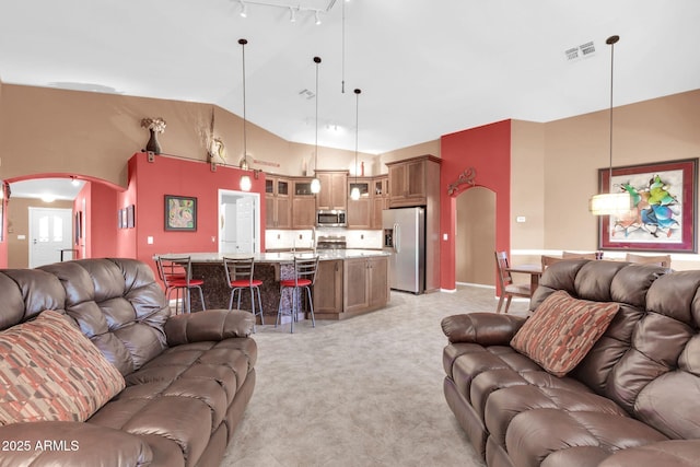 living room featuring track lighting, visible vents, arched walkways, and high vaulted ceiling