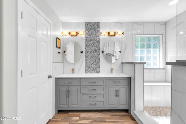 full bathroom with walk in shower, double vanity, wood finished floors, tile walls, and a sink