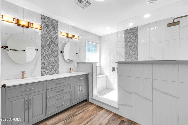 bathroom with visible vents, a walk in shower, a sink, wood finished floors, and tile walls