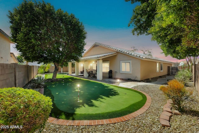 back of property at dusk with a tile roof, a patio area, a fenced backyard, and stucco siding