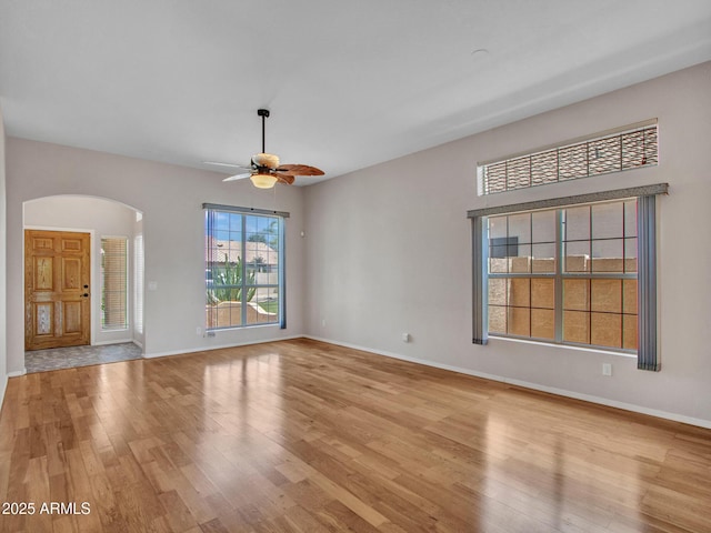 11547 W King Snake Ct, Surprise, AZ 85378 - unfurnished living room with arched walkways, light wood-style floors, a ceiling fan, and baseboards
