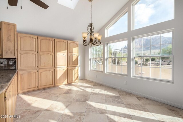 unfurnished dining area featuring ceiling fan with notable chandelier, high vaulted ceiling, and a skylight