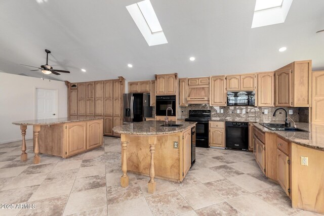 kitchen with a breakfast bar, sink, light stone counters, black appliances, and a center island with sink