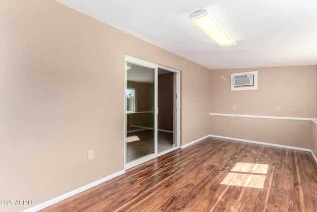 empty room with a wall mounted air conditioner, baseboards, and wood finished floors