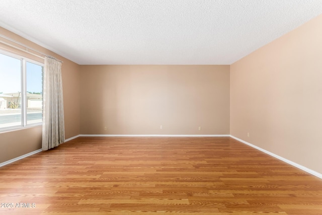 unfurnished room with baseboards, a textured ceiling, and light wood finished floors