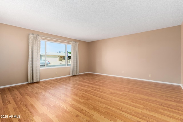 spare room with light wood-type flooring, baseboards, and a textured ceiling