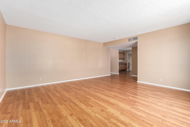 spare room featuring light wood-type flooring, baseboards, visible vents, and a textured ceiling