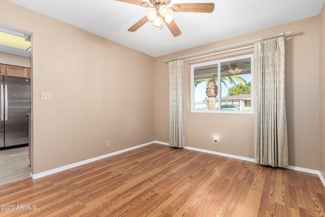 unfurnished room with a ceiling fan, light wood-style flooring, baseboards, and a textured ceiling