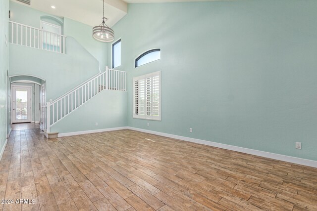 unfurnished living room featuring light hardwood / wood-style flooring, a chandelier, and high vaulted ceiling