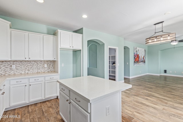 kitchen with a center island, hanging light fixtures, white cabinets, decorative backsplash, and light hardwood / wood-style flooring