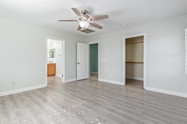 unfurnished bedroom featuring a walk in closet, ensuite bathroom, light wood-type flooring, and ceiling fan