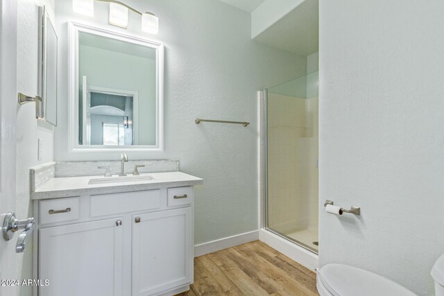 bathroom featuring toilet, hardwood / wood-style flooring, a shower with shower door, and vanity