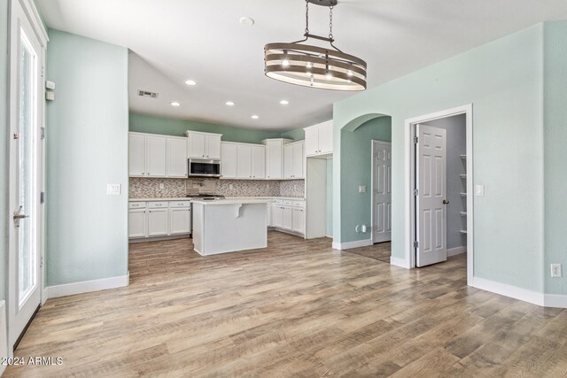 kitchen with light hardwood / wood-style flooring, a center island, decorative light fixtures, white cabinetry, and tasteful backsplash