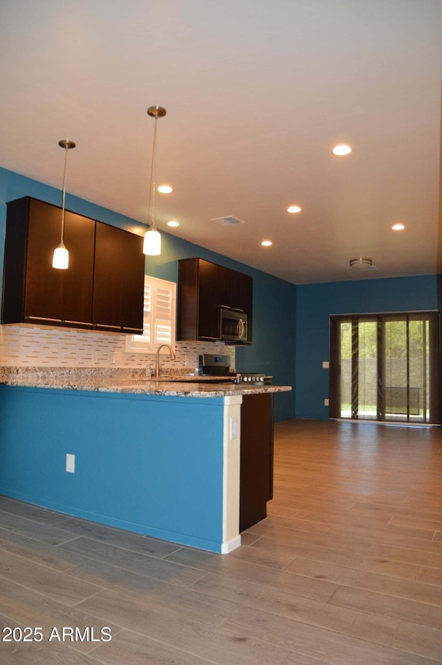 728 S Meadowood Ln, Sierra Vista, AZ 85635 - kitchen featuring stainless steel microwave, tasteful backsplash, wood finished floors, dark brown cabinets, and light stone counters