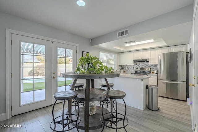 kitchen featuring french doors, appliances with stainless steel finishes, a tray ceiling, decorative backsplash, and white cabinets