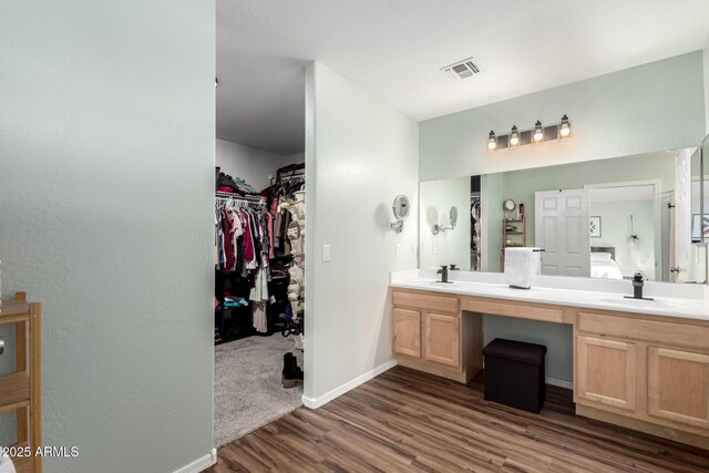 ensuite bathroom featuring double vanity, visible vents, a spacious closet, a sink, and wood finished floors