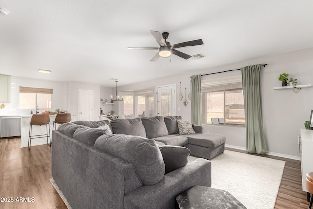 living room featuring visible vents, baseboards, wood finished floors, and ceiling fan with notable chandelier