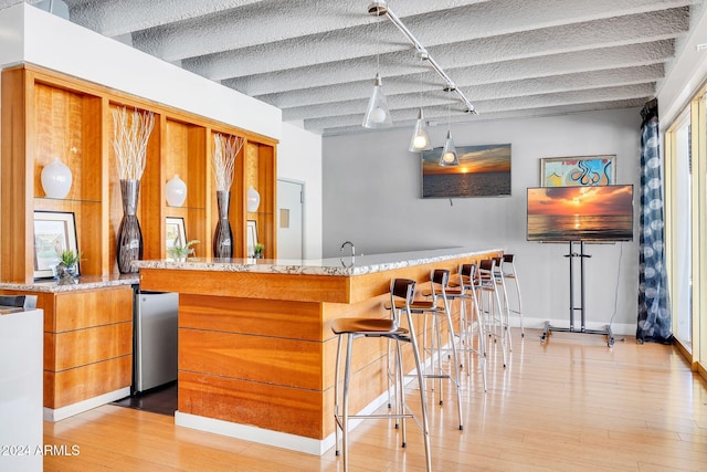 bar with decorative light fixtures, light hardwood / wood-style floors, and light stone countertops