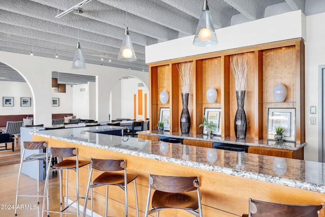 kitchen with kitchen peninsula, beam ceiling, light hardwood / wood-style floors, and light stone counters