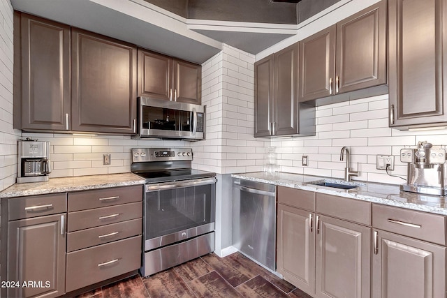 kitchen featuring decorative backsplash, light stone countertops, stainless steel appliances, dark wood-type flooring, and sink