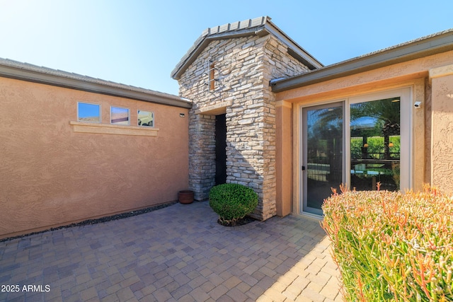 property entrance with a patio area, stone siding, and stucco siding