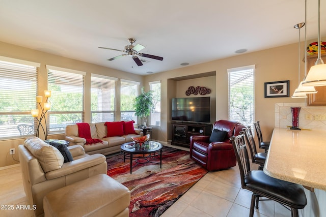 living area featuring light tile patterned floors, a healthy amount of sunlight, baseboards, and ceiling fan