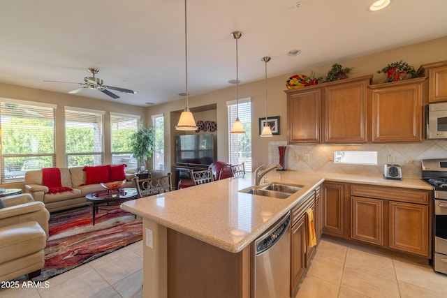 kitchen with stainless steel appliances, decorative backsplash, a sink, open floor plan, and brown cabinets