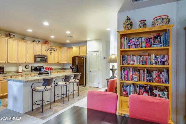 kitchen featuring light brown cabinetry, a breakfast bar, an island with sink, recessed lighting, and black appliances