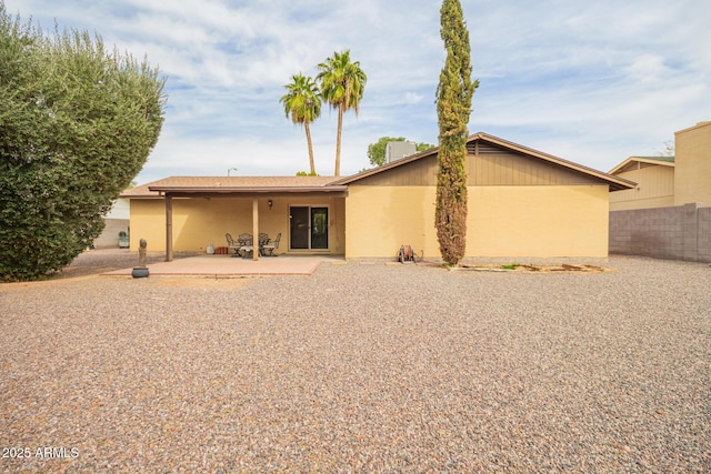 rear view of house with a patio area, fence, and stucco siding