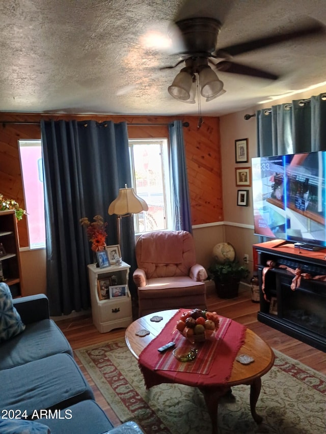 living room featuring wood walls, wood-type flooring, a textured ceiling, and ceiling fan