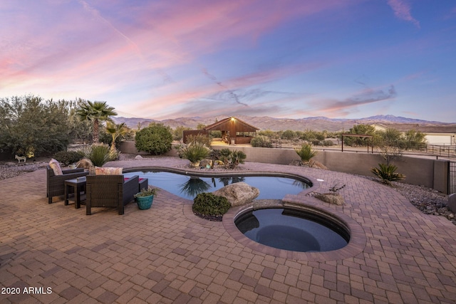 pool at dusk with an in ground hot tub, a mountain view, and a patio