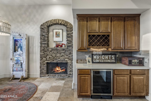 bar with wine cooler, decorative backsplash, and a stone fireplace