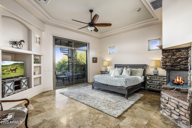 bedroom with a tray ceiling, access to exterior, ceiling fan, and a stone fireplace