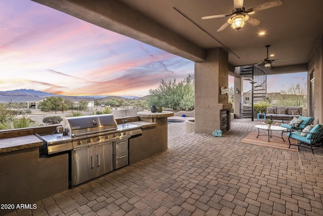 patio terrace at dusk featuring a mountain view, an outdoor kitchen, an outdoor hangout area, and ceiling fan