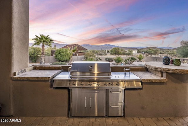 patio terrace at dusk with a mountain view, a grill, and an outdoor kitchen