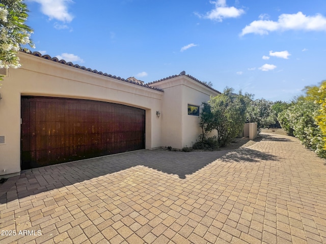 view of home's exterior with an attached garage, decorative driveway, stucco siding, and a tile roof