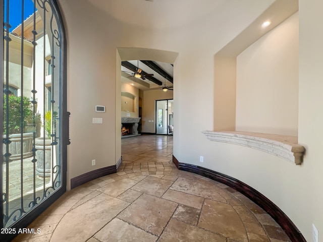 foyer with baseboards, a warm lit fireplace, beam ceiling, and stone tile floors
