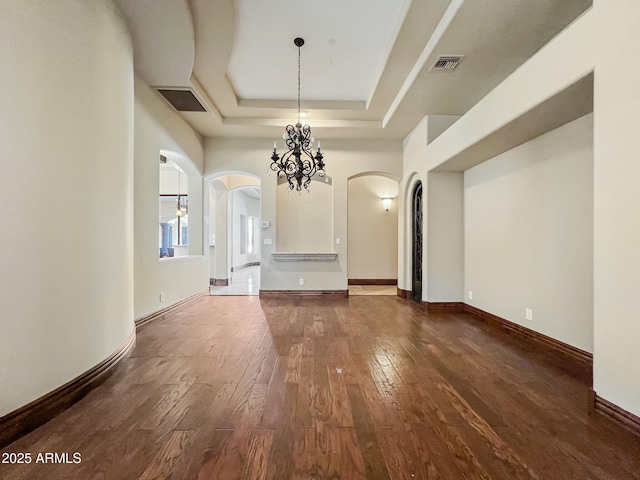 unfurnished dining area with arched walkways, visible vents, a raised ceiling, and dark wood-type flooring