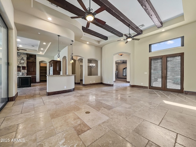 unfurnished living room with arched walkways, a high ceiling, a ceiling fan, and stone tile floors