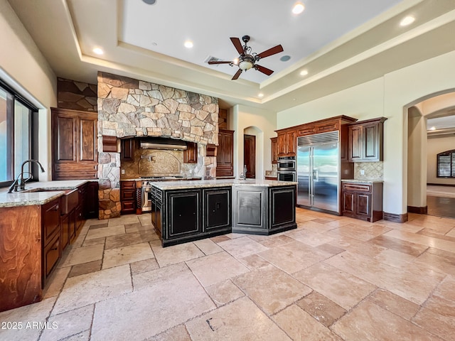 kitchen with a sink, arched walkways, high quality appliances, and a raised ceiling