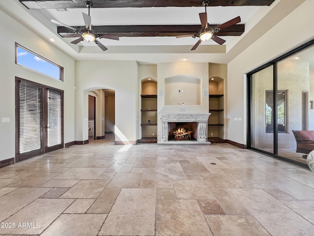 unfurnished living room featuring ceiling fan, arched walkways, built in shelves, baseboards, and stone tile floors