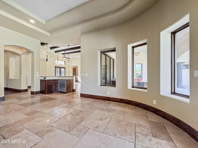 unfurnished living room with stone tile floors, a towering ceiling, baseboards, recessed lighting, and arched walkways