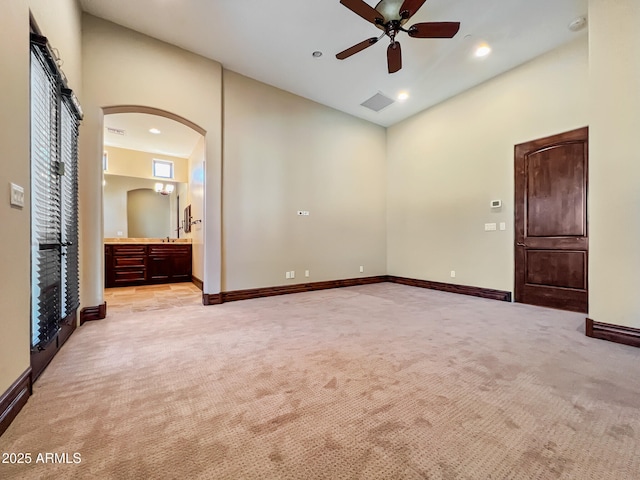 spare room featuring ceiling fan, light colored carpet, arched walkways, baseboards, and visible vents