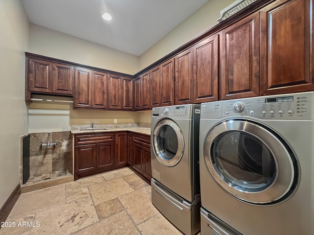 washroom with stone tile flooring, washer and dryer, baseboards, a sink, and cabinet space