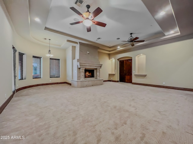unfurnished living room featuring visible vents, arched walkways, ceiling fan, and a tray ceiling