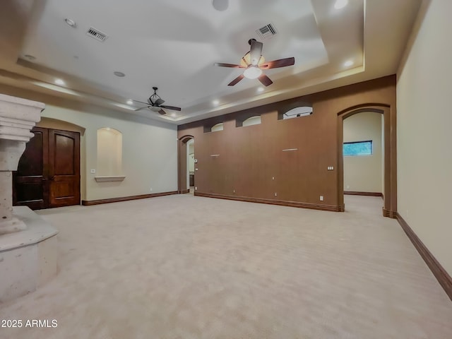 unfurnished living room featuring arched walkways, a tray ceiling, visible vents, and ceiling fan